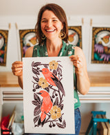 Woman holding a print of two birds and flowers in an art studio.
