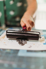 A hand rolling black ink onto a wood block in preparation to make a print. 