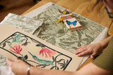 Person holding a floral design on a table with patterned fabric and a butterfly book.