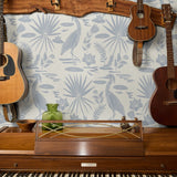 Tropical pattern with palm fronds, herons, and foliage in soft blue-gray on cream background