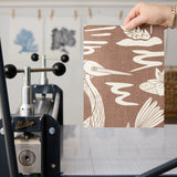 Tropical bird and palm leaf pattern in cream on terracotta brown background