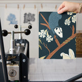 Dark floral pattern with cream magnolias, blue berries, green leaves and brown branches on black bac