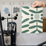 Geometric botanical pattern with teal green leaves, circles, and gray squares on cream background