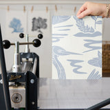 Tropical pattern with palm fronds, herons, and foliage in soft blue-gray on cream background