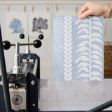 Blue and white vertical stripe pattern with leaf motifs and textured linen background