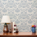 Symmetrical botanical pattern with stylized flowers, leaves, and moths in soft blue-gray on cream ba