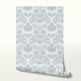 Symmetrical botanical pattern with stylized flowers, leaves, and moths in soft blue-gray on cream ba